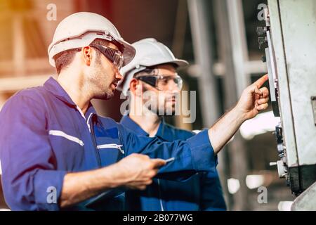 industry engineer team worker teaching help friend operate control heavy machine in factory Stock Photo