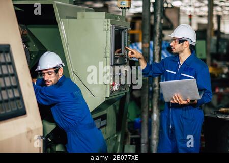Machine service team checking CNC and re-programming process during factory production. Stock Photo