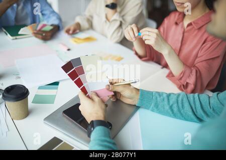 Close-up of male designer holding colored palette in his hands while sitting at the table with tablet pc and business people Stock Photo