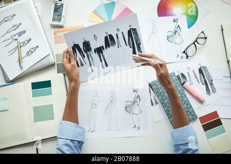 Close-up of male designer pointing at sketches of clothes while working at his workplace at office Stock Photo