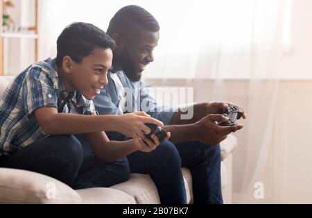 Afro father and son playing video games with joysticks Stock Photo