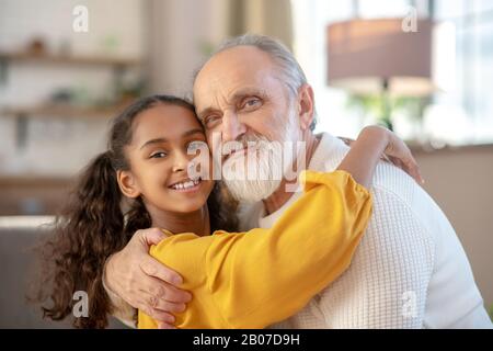 Grey-haired man and a dark-skinned girl hugging each other Stock Photo