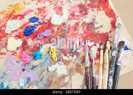 Close-up of palette with paints and different paintbrushes on the table in workshop Stock Photo