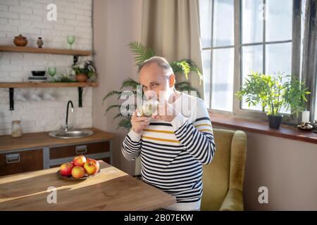 Bearded grey-haired man in a striped sweater having tea at home Stock Photo