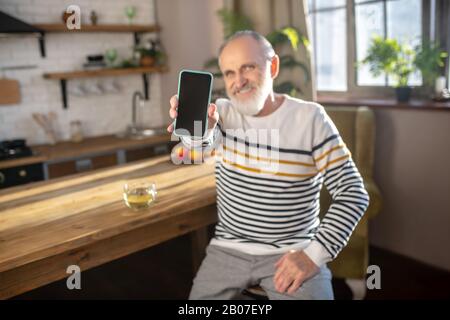 Bearded grey-haired man in a striped sweater sitting in the kitchen Stock Photo