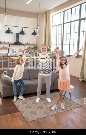 Bearded grey-haired man dancing with his granddaughters Stock Photo