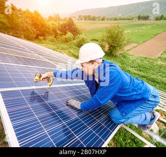 Construction worker connects photo voltaic panel to solar system using screwdriver. Professional installing and construction of solar system, alternative energy and financial investment concept. Stock Photo