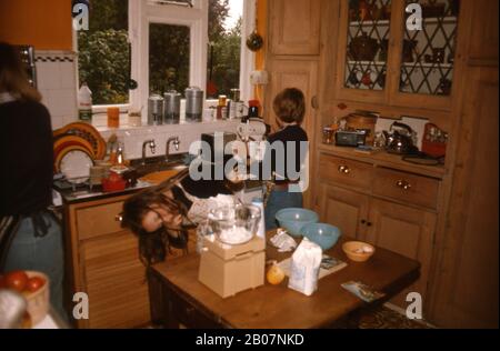A mother and two kids baking cakes in their kitchen UK 1973 Stock Photo
