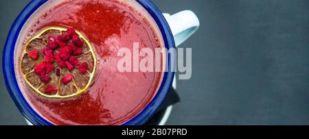 Fresh healthy berry juicy smoothies with red cranberries, currants, goji berries, decorated with orange slice on grey wooden background. Detox drink rich in vitamin. Top view Stock Photo