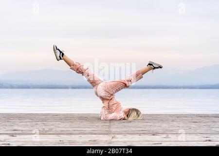 A beautiful woman performs the exercises lifting her legs to the top, lake, pier, Fitness. Sport. Yoga. Stock Photo