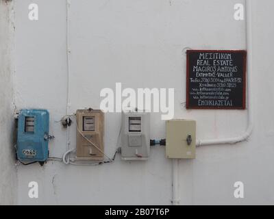 Electricity meters on a wall in Kalamos, Kythira, Greece, painted in three different colours. Next to an advertising sign for a real estate company. Stock Photo