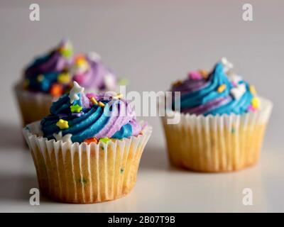 3 vanilla cupcakes with purple and blue frosting with confetti sprinkles on a white background, perfect delicious treat for a birthday or celebration! Stock Photo
