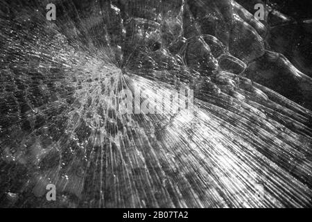 Abstract texture of a broken glass sheet over dark stone background. Black and white photo