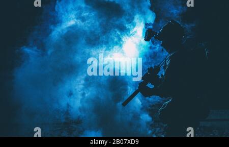 Silhouette of modern infantry soldier, elite army fighter in tactical ammunition and helmet, standing with assault service rifle in hands in the smoke Stock Photo