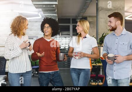 Group of young cheerful coworkers drinking coffee and talking Stock Photo