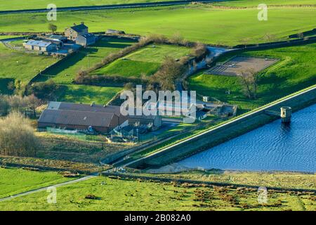 High sunny rural view of farm fields, embankment wall, dam, valve tower & water treatment works at Embsay Reservoir - North Yorkshire, England, UK.