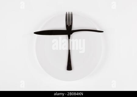 Cutlery language, dining etiquette. Ready for the second meal. White ceramic round plate with knife anf fork isolated on white, top view. Stock Photo