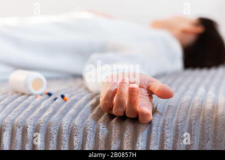 Woman’s hand close up committing suicide by overdosing on medication, pills and bottle beside. Overdose pills and addict concept background Stock Photo