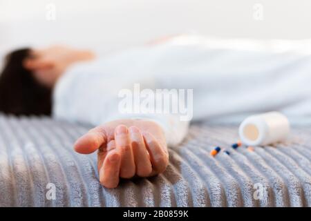 Woman’s hand close up committing suicide by overdosing on medication, pills and bottle beside. Overdose pills and addict concept background Stock Photo