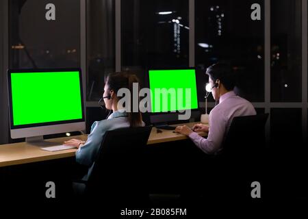 Late Night Environment. Rear view young adult friendly Call centre operator with headsets working hard at night. Using for 24 Hr. 7 days Call center C Stock Photo