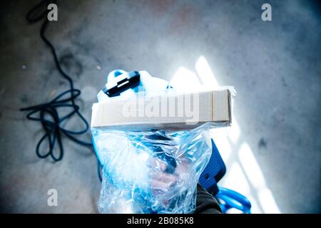 Overhead view of male hand holding new unboxed unpacked vacuum cleaner professional brush used in construction industry - background of concrete construction site Stock Photo