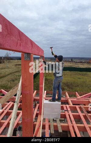 Rafters wooden against the blue sky, the master is working on the installation of bars. Stock Photo