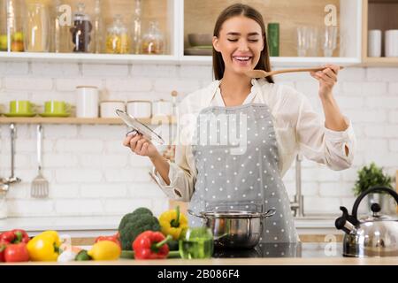 Happy woman tasting soup from wooden spoon Stock Photo