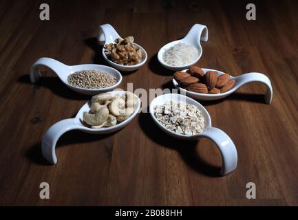 Ingredients for Vegan Milk for self production, arranged on a wooden plate in white bowls, almond, walnut, rice, oat flakes, cashew nuts, sesams Stock Photo