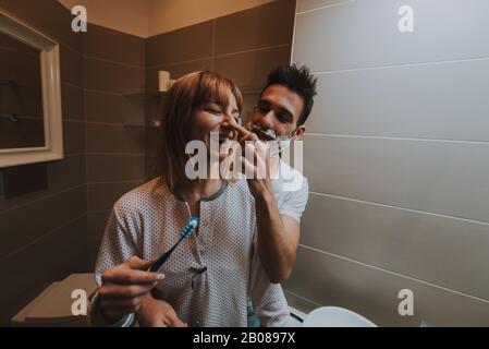 Couple morning routine. Man and woman sharing bathroom. Shaving beard and brushing teeth Stock Photo