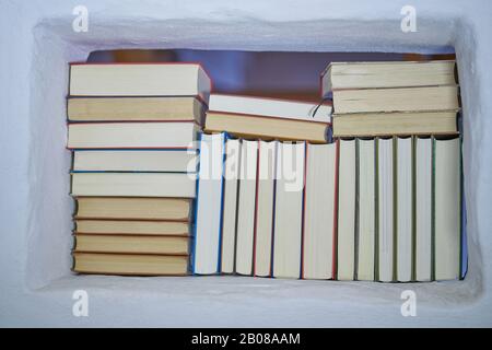 Back of assortment of books in a white shelf with view to the next room in a white textured wall, closeup Stock Photo