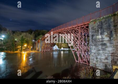 Ironbridge, UK. 18th Feb 2020. As flood levels on the River Severn reached their peak in the early hours of Tuesday 18th February 2020, residents of Ironbridge waited to see if flood defences would withstand the 470 tonnes per second of water flowing through the Ironbridge Gorge World Heritage Site. The long exposure creates a millpond effect to the raging torrent of swirling eddies passing under the historic Ironbridge which had already flooded numerous properties along the River Severn in Shropshire. Credit: Paul Bunch/Alamy Live News. Stock Photo