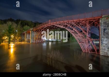 Ironbridge, UK. 18th Feb 2020. As flood levels on the River Severn reached their peak in the early hours of Tuesday 18th February 2020, residents of Ironbridge waited to see if flood defences would withstand the 470 tonnes per second of water flowing through the Ironbridge Gorge World Heritage Site. The long exposure creates a millpond effect to the raging torrent of swirling eddies passing under the historic Ironbridge which had already flooded numerous properties along the River Severn in Shropshire. Credit: Paul Bunch/Alamy Live News. Stock Photo