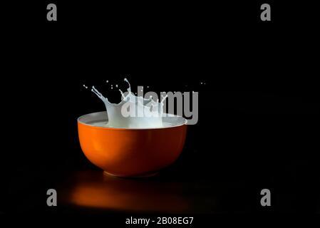 crown of splashed milk in a red bowl - high speed image isolated on black background Stock Photo