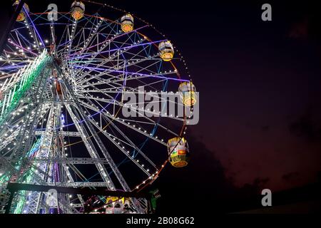 Giant Ferris Wheel with well illuminated cabins and decorated with colorful lights during night, Stock Photo