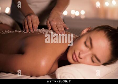 Beauty therapist pouring salt scrub on womans back Stock Photo