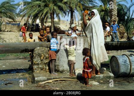 TUNISIA, SAHARA DESERT, OASIS, WOMAN DRAWING WATER FROM WELL Stock Photo