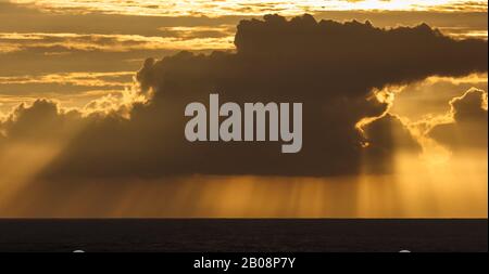 Crepuscular rays of the setting sun stream through a dark monsoon cloud bank hanging above the sea off the coast in Gokarna in India. Stock Photo