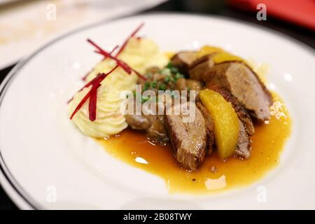 Roasted duck topped with orange sauce and mashed potatoes Decorate the dish looks appetizing on the white plate in the restaurant. Selective focus. Stock Photo