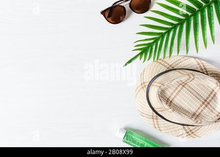 Summer composition with straw hat, sunglasses, palm leaf and sun protection oil on white wooden background top view. Summer fashion, vacation concept. Stock Photo