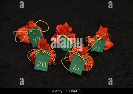 Twenty four little presents wrapped in red, green tags golden numbers from 1 to 24 on black as self made advent calendar - 20th of December Stock Photo