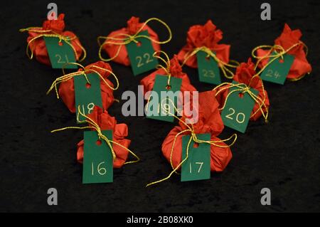 Twenty four little presents wrapped in red, green tags golden numbers from 1 to 24 on black as self made advent calendar - 16th of December Stock Photo