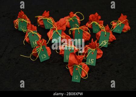 Twenty four little presents wrapped in red, green tags golden numbers from 1 to 24 on black as self made advent calendar - 12th of December Stock Photo