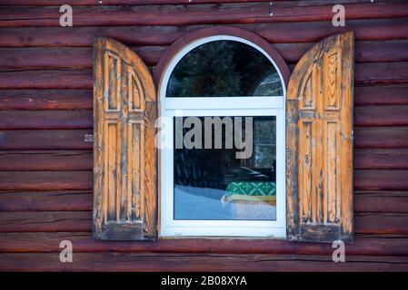 A window with wooden shutters against a cherry wood wall.  Stock Photo