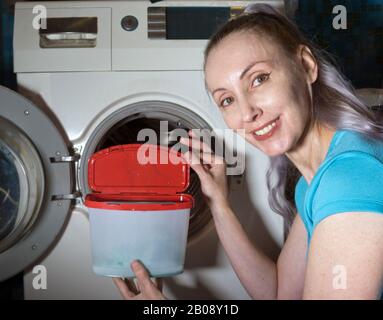 joyful woman in the background of a washing machine holds a box with washing gel in her hands, photo from the series Stock Photo