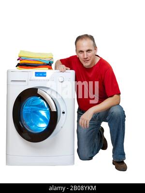 smiling man near the washing machine and a stack of bright linen, isolated on white background Stock Photo