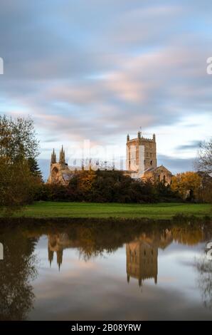 Tewkesbury Abbey, in Worcestershire lit by the setting sun at golden hour during and reflecting in the floodwater of the 2019 floods Stock Photo