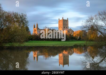 Tewkesbury Abbey, in Worcestershire lit by the setting sun at golden hour during and reflecting in the floodwater of the 2019 floods Stock Photo