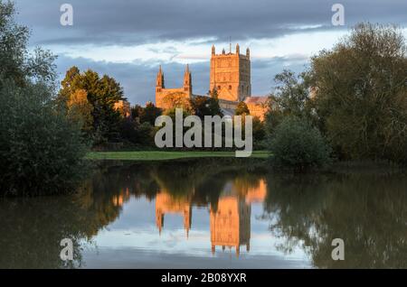 Tewkesbury Abbey, in Worcestershire lit by the setting sun at golden hour during and reflecting in the floodwater of the 2019 floods Stock Photo