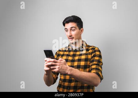 unbelievable happy news. surprised man in yellow shirt holding a phone Stock Photo