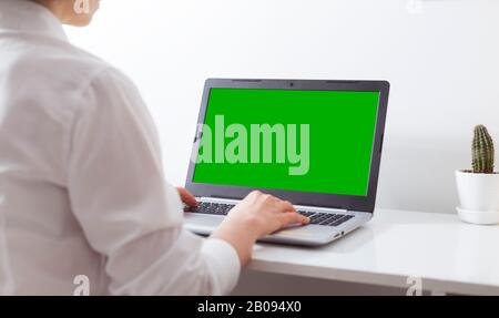 A woman works in a white office at a laptop with a green screen. Stock Photo